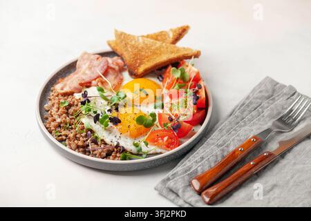Gesundes Frühstück - Eier, Toast, Buchweizen, Speck, Bohnen und Tomaten auf einem Teller auf dem Tisch. Stockfoto