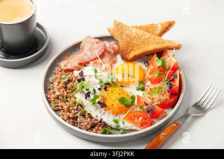 Gesundes Frühstück - Eier, Toast, Buchweizen, Speck, Bohnen und Tomaten auf einem Teller auf dem Tisch. Stockfoto