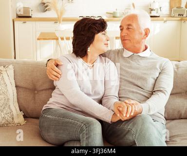 Reifes 60-jähriges Paar umarmt sich, während es auf dem Sofa sitzt. Liebe für immer. Stockfoto