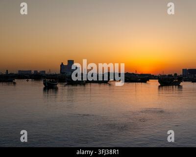 Silhouette von traditionellen Holz-Dhow-Booten, die in der Bucht bei Sonnenaufgang entlang der Doha Corniche in Katar vor Anker liegen. Stockfoto