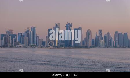Panoramablick auf die moderne Skyline von Doha West Bay über ruhige Buchtgewässer während einer weichen violetten Dämmerung in Katar. Stockfoto