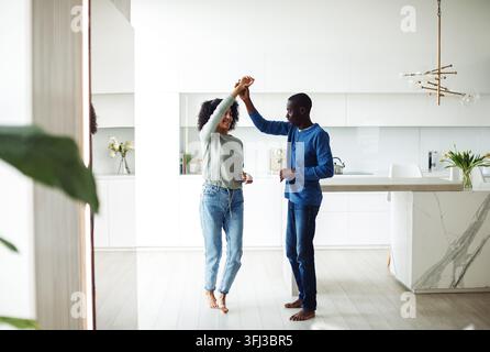 Fröhliches schwarzes Paar tanzt zur Musik in einem modernen Kücheninterieur. Stockfoto