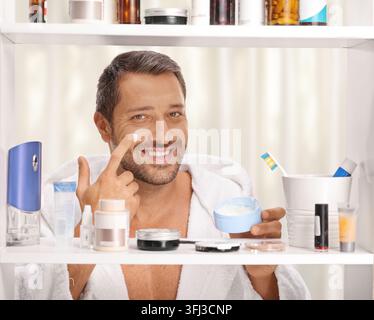 Lächelnder Mann, der vor einem Badezimmerschrank Gesichtscreme aufträgt Stockfoto