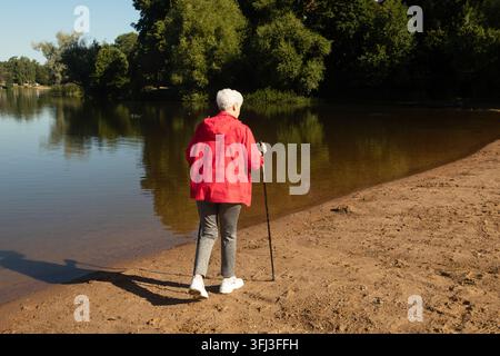 Rückansicht einer sportlichen älteren Frau, die Ausdauer trainiert, während sie im Freien Nordic Walking macht Stockfoto