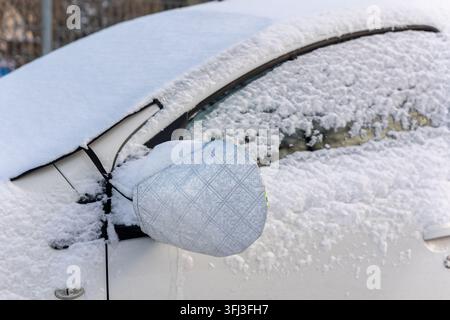 Schneebedecktes Auto verwendet reflektierende Spiegelabdeckung und Windschutzscheibenprotektor, um Frost- und Eisbildung im Winter zu verhindern. Schutzzubehör hilft Stockfoto