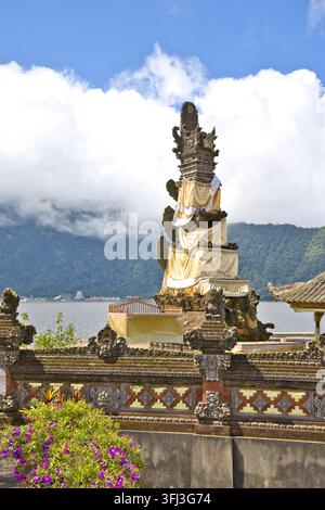 Lebendige rote Canna-Lilienblüten im Vordergrund rahmen die berühmten schwimmenden Meru-Türme des Pura Ulun Danu Bratan Tempels am See Stockfoto