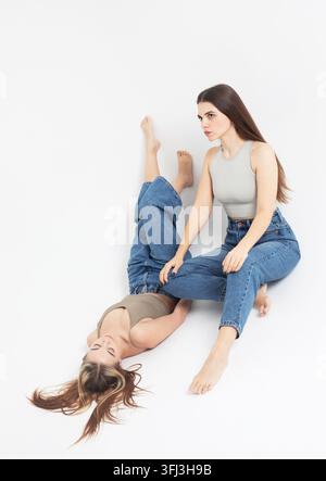 Zwei modebewusste lachende Freundinnen, die auf dem Boden sitzen Stockfoto