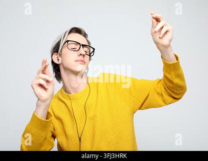 Stylischer modischer junger Mann trägt einen gelben Pullover mit Kopfhörern und tanzt zur Musik Stockfoto