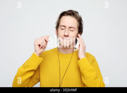 Stylischer modischer junger Mann trägt einen gelben Pullover mit Kopfhörern und tanzt zur Musik Stockfoto