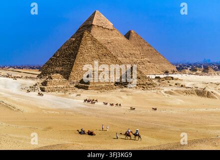 Luftaufnahme von Kamelkarawanen, die auf die Giza-Nekropole zusteuern (die Pyramide von Khafre, die Pyramide von Khufu und die Pyramiden der Königinnen), Giza, Kairo, Ägypten Stockfoto