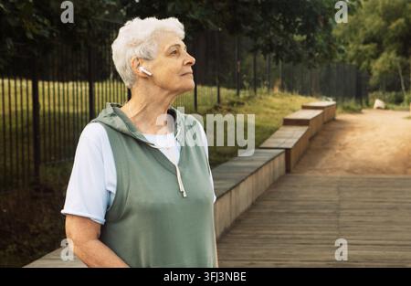 Eine ältere Frau mit kurzen lockigen Haaren geht in einem Sommerpark. Stockfoto