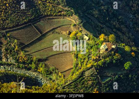 Luftaufnahme von Terrassenfeldern und einem kleinen ländlichen Weiler an einem Hang, Herbstlaub, ein Bach fließt unten in der Berglandschaft. Albanien, Europa Stockfoto