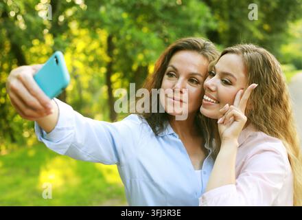 Reife Mutter und erwachsene Tochter machen ein Selfie mit dem Mobiltelefon im Sommerpark Stockfoto