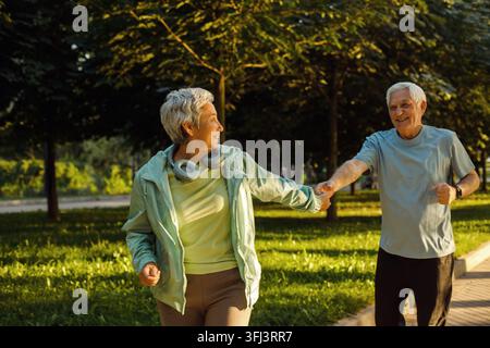 Senioren-Paar läuft zusammen im Park und schaut sich beim Joggen und Schlankheitsübungen an. Stockfoto