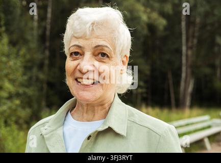 Porträt einer lächelnden älteren Frau im Park. Nahaufnahme-Porträt. Glückliche, nachdenkliche reife Frau, die im Freien entspannt. Stockfoto