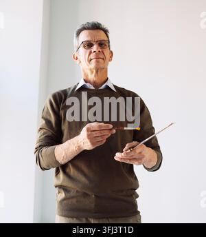 Ein fünfzigjähriger Mann hält eine Palette mit Farben und Pinseln in seinen Händen. Stockfoto