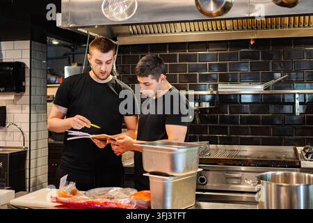 Zwei Köche diskutieren die Speisekarte in einer professionellen Restaurantküche Stockfoto
