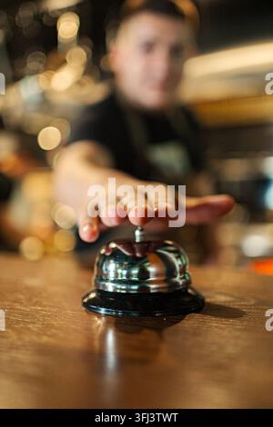 Hand drückt Serviceglocke auf Holztheke in Bar oder Restaurant Stockfoto