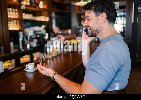 Junger Erwachsener sitzt an der Theke in einem Café und telefoniert mit dem Mobiltelefon Stockfoto