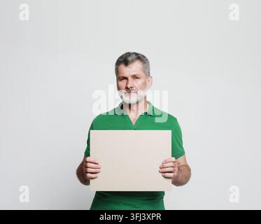 Ein gealterter attraktiver bärtiger Mann hält ein Schild in den Händen und zeigt mit dem Finger darauf. Präsentation, Werbung. Stockfoto