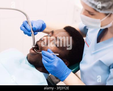 Porträt eines schwarzen männlichen Patienten, der in einer modernen Klinik eine Zahnbehandlung mit einem Zahnarzt erhält, sitzend auf einem Stuhl in einem weißen Kabinett. professioneller Stomatologe fe Stockfoto