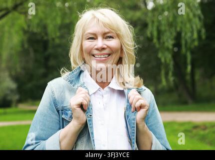 Schöne blonde Frau in einer Jeansjacke in einem Frühlingspark. Ältere glückliche Dame Rentnerin. Nahaufnahme. Stockfoto