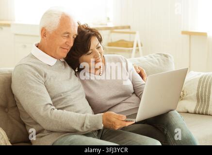 Seniorenpaar, das einen Laptop-Computer benutzt und auf dem Sofa zu Hause sitzt Stockfoto