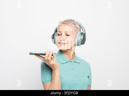 Lächelnde reife Frau mit Kopfhörern und kurzen Haaren, die eine Sprachnachricht am Telefon aufnimmt, Nahaufnahme Stockfoto