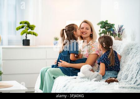 Mutter, die einen Kuss von ihrer Tochter erhält, während sie auf der Couch sitzt Stockfoto
