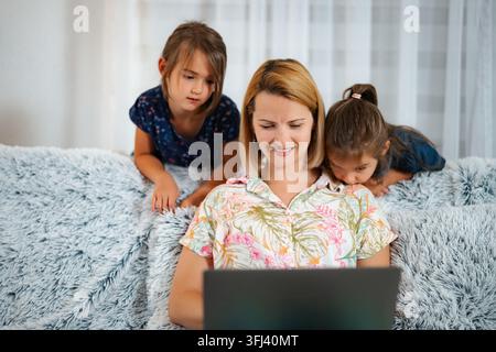Mutter verwendet einen Laptop auf dem Sofa, während Kinder über ihre Schultern schauen Stockfoto