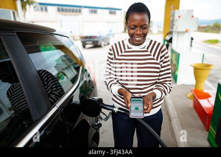 Frau tankt Auto und nutzt ein Smartphone für die kontaktlose Zahlung an einer Tankstelle Stockfoto
