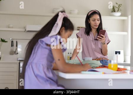Afroamerikanische Mutter und Tochter lehnen sich an Kücheninsel, überprüfen Handy, zeichnen, Kopierraum. Zuhause, Familie, Studium, Kunst, c Stockfoto