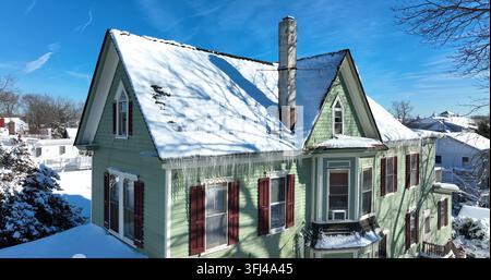 Eiszapfen im Winter Schnee tropfen vom Hausdachvorsprung. Hübsche grüne Verkleidung. Blauer Himmel. Familienhaus, Cape May, New Jersey. Stockfoto