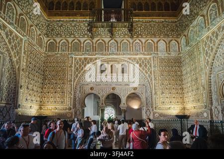 Sevilla, Spanien - 09. Apr. 2025: Touristen versammeln sich unter den reich vergoldeten Mudejar-Stuckarbeiten und geschnitzten Bögen einer großen Halle im Real Alcazar-Palast Stockfoto