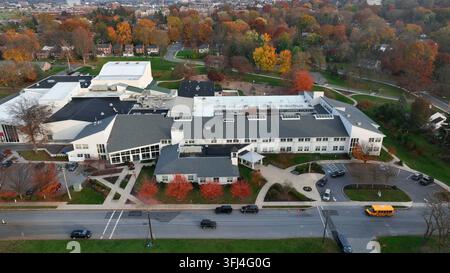 Amerikanisches Highschool-Gebäude und Schulbus, der auf der Straße geparkt ist. Luftaufnahme mit einem Lastwagen in farbenfrohem Herbstlaub in den USA, Lancaster, Pennsylvania. Stockfoto