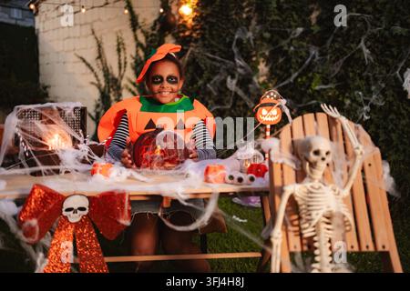 Mädchen feiert Halloween in einem Kürbiskostüm und mit Skelett-Make-up Stockfoto