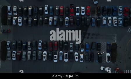 Luftaufnahme von oben über einen dunklen Parkplatz voller Autos und geschäftig mit Autos, die Parkplätze betreten und verlassen, Lancaster, Pennsylvania. Stockfoto