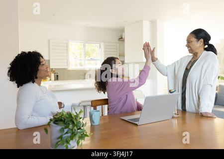 Afroamerikanische Familie, Teenager-Tochter gibt einer Seniorin in der Küche mit Laptop einen Highfive Stockfoto