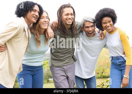 Verschiedene Freunde, die auf einem grasbewachsenen Hügel posieren und sich nach vorne lehnen, Jeans und Armbanduhr tragen. Draußen, Gruppe, Kameradschaft, Wiese, Grün, Denim, c Stockfoto