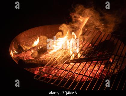 Loderndes Holzfeuer mit glühenden Kohlen in einem Barbecue-Grill bei Nacht Stockfoto
