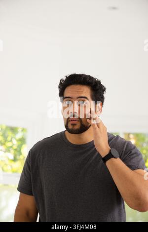 Mittelalter Afrikaner berührt seine Wange und schaut nach oben in einem hellen Raum mit Smartwatch. Porträt, männlich, Wearable, minimalistisch, Innenraum, Fenster, grün Stockfoto