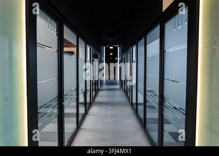 Moderner Bürokorridor mit Glastüren und linearer Beleuchtung Stockfoto