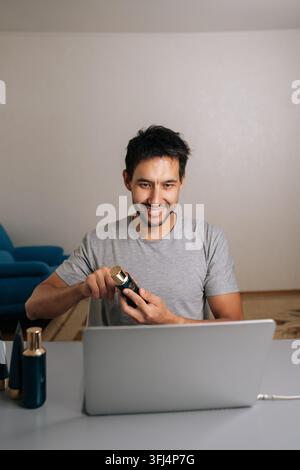 Vertikales Porträt eines lächelnden Mannes, der über Schönheit und Hautpflege vloggt, Online-Rezension von Kosmetikprodukten mit einem Laptop durchführt und mit dem Publikum interagiert Stockfoto