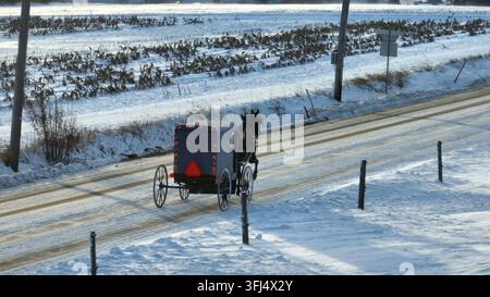 Amische Pferdekutsche auf ländlicher Straße mit Schnee im Winter. Amische Gegend in den USA während eines Schneesturms, Strasburg, Pennsylvania. Stockfoto