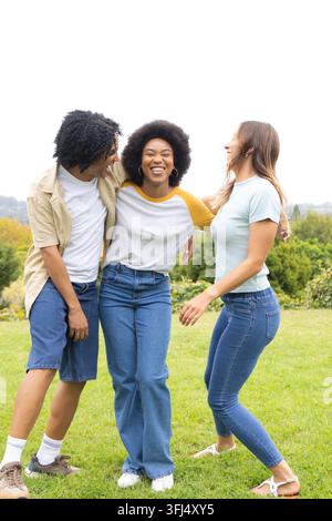 Verschiedene Freunde stehen mit den Armen um die Schultern auf einem grasbewachsenen Hang, lächeln und tragen Jeans. Draußen, Park, Wiese, Gruppe, lässig, natürlich, Natur Stockfoto