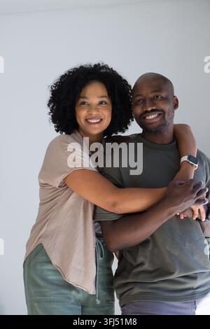 Afroamerikanisches Paar umarmt sich, lächelt an einer hellgrauen Wand, Mann in olivgrünem T-Shirt mit Smartwatch. Zuneigung, Umarmung, Wärme, lässig, minimalistisch, Leben Stockfoto