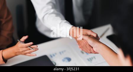 Hohe Winkelansicht von Geschäftspartnern, die sich über Dokumenten und Finanzberichten an einem Bürotisch während einer erfolgreichen Strategiesitzung die Hände schütteln. Stockfoto