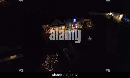Dekorierte Weihnachtshaus bei Nacht in den USA. Luftaufnahme, Annäherung. Festlicher Vorgarten und beleuchteter Stern im Fenster. Friedliche Wohngegend der Vereinigten Staaten Stockfoto