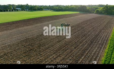 Luftaufnahme, die sich zurückzieht, von einem Amische-Mann, der ein Feld bepflanzt. Sechs Arbeitspferde ziehen einen John-Deere-Pflanzmaschine. Sonnenuntergang an einem Frühlingstag, Bird-in-Hand, Pennsylvania. Stockfoto