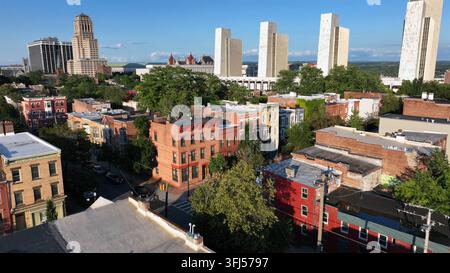 Flug in niedriger Höhe über Dächer von Backsteinhäusern und Wohnhäusern in der Innenstadt von Albany. Sonnenuntergangzeit. Moderne Gebäude am Empire State Plaza in der Ferne, Stadt von Stockfoto